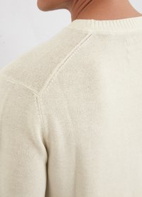 Light beige knitted sweater with a round neckline, featuring fine ribbed detailing at the collar and shoulder seams. Smooth texture.