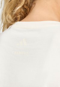 Witte sportshirt met een gladde textuur. Heeft een subtiele, reliëf Adidas-logo en de tekst "LES MILLS" in dezelfde kleur op de rug.