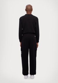 Zwart sweatshirt en cargobroek set, met cargopockets, geribde manchetten en logo-details. Soepele textuur, ontspannen pasvorm en bijpassende schoenen.