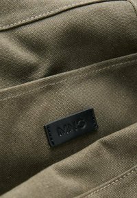 Tessuto verde oliva con finitura testurizzata, caratterizzato da molteplici tasche e un'etichetta in pelle nera impresso con "MNG."