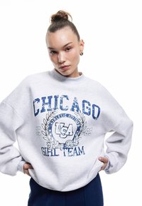 Grå sweatshirt med ribbet halsudskæring og løs pasform. Har blå grafisk tekst: "Chicago," "USA," og "Finley Park Girl Team."