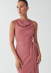 Sleeveless pink dress featuring a draped neckline, a fitted bodice, and a tied waist detail, made from a smooth, lightweight fabric.