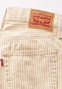 Poche arrière de jean Levi's beige et blanche rayée avec étiquette rouge Levi's et patch en cuir marron au-dessus de la poche.