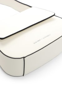 Bolso cruzado de cuero blanco con ribete negro, que cuenta con un cierre de solapa magnético y un logo en relieve en el frente. Diseño suave y estructurado.