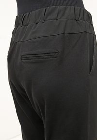 Pantalones elásticos negros con una textura suave, que cuentan con una amplia cinturilla elástica y un bolsillo trasero con un sutil borde cosido.