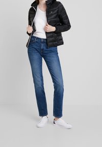 Czarna kurtka puchowa z kapturem, biały zamek, biały T-shirt, niebieskie dżinsy i białe trampki. Prosty design, gładka faktura, swobodny krój.