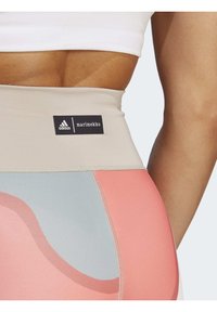 Legginsy z wysokim stanem w różowe i niebieskie abstrakcyjne wzory, wykonane z elastycznego materiału. Zawierają czarną metkę Adidas x Marimekko.