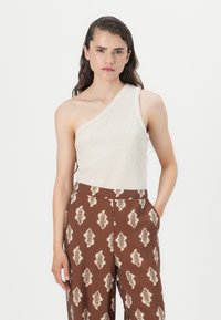 Utsmykket kremfarget ribbet tanktopp med asymmetrisk design og én skulder. Kombinert med brune vide bukser med mønster som har bladdesign i kremfarge.