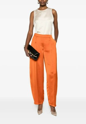 Donna che indossa un top in raso bianco senza maniche, pantaloni larghi a vita alta in raso arancione, décolleté beige con punta, tenendo una pochette nera.