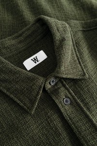 Donkergroene, gestructureerde polo met een kraag, voorzien van twee zwarte knopen en een wit label met een logo.