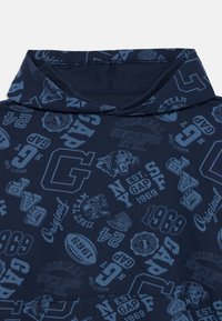 Felpa blu navy con loghi e testi sportivi di colore azzurro su tutta la superficie, tra cui "GAP," "1969," un pantera ruggente e "Original."
