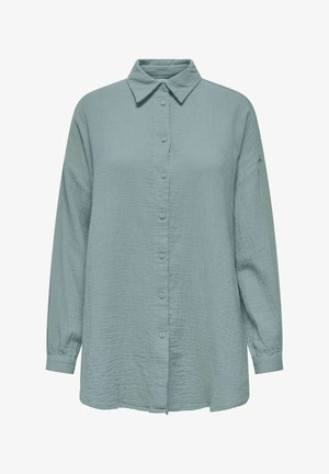 Chemise à manches longues, boutonnée, de couleur vert sauge clair avec un tissu texturé et un col pointu, présentée sur un fond blanc.