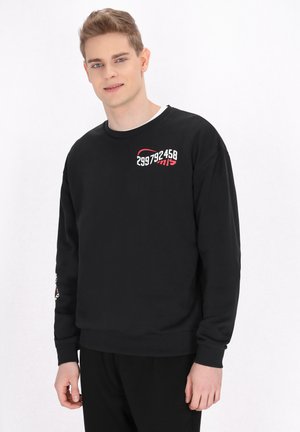 Sort sweatshirts med rund hals, lange ærmer. Har hvid og rød print på brystet og venstre ærme. Blødt stof, afslappet pasform.