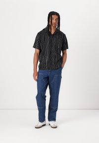 Short-sleeve black shirt with white vertical stripes, front pocket, paired with loose-fitting blue denim jeans and white sneakers.