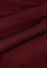 Burgundia kangas, millel on õrn ribikate tekstuur, näitab pehmeid voldikuid ja kerget läiget, rõhutades selle siledat ja vastupidavat materjali.