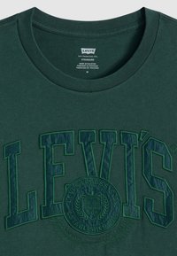 Tamsiai žalia medvilninė marškinėlių su dideliu iškilniu "LEVI'S" logotipu ir apvaliu emblemu priekyje, su klasikinio apvalaus kaklo dizainu.