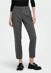 Pantaloni grigi su misura in un tessuto testurizzato, con una vestibilità slim e una leggera affusolatura alla caviglia, abbinati a mocassini neri con accenti dorati.