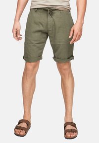 Short en lin vert olive avec revers roulés, taille à cordon et poches avant. Associé à des sandales marron avec des brides réglables.