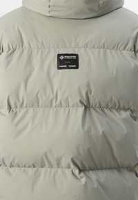 Lysegrøn pufferjakke med et kviltet design, der har et Windstopper-label, samt en høj krave for ekstra varme og beskyttelse.