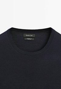 Maglione girocollo blu scuro realizzato in 100% lana merino, con una texture a costine e un'etichetta con il marchio e le istruzioni per la cura.