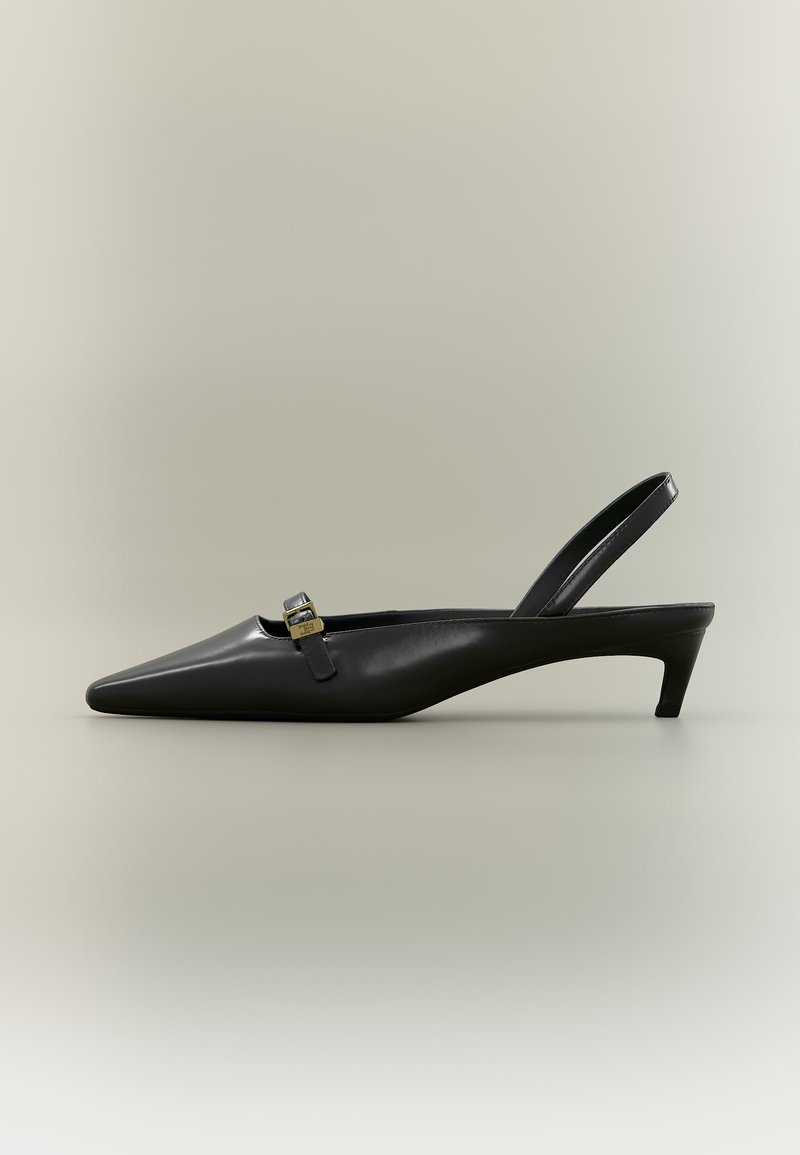 Escarpin slingback en cuir noir avec talon kitten, bout pointu et petite boucle dorée sur un fond uni.