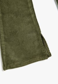 Oliivinvihreät corduroy-housut, joissa on pehmeä tekstuuri, suora leikkaus ja sivureiät helmassa. Näkyvää ompelua reunojen ympärillä.