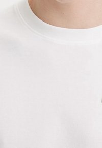 Biała bawełniana koszulka z okrągłym dekoltem i krótkimi rękawami. Gładka tekstura, standardowy krój, minimalne detale szwów na kołnierzyku.