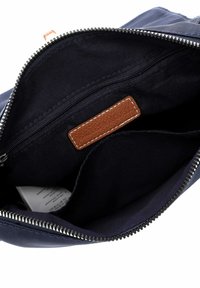 Sac bleu marine ouvert montrant l'intérieur en tissu noir avec une poche zippée et une étiquette de marque en cuir marron cousue à l'intérieur.