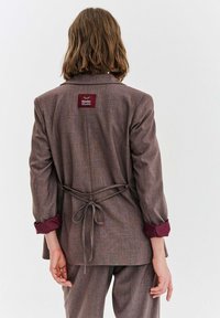 Brązowa, dopasowana marynarka ze śliwkowymi mankietami i wiązaniem w talii. Posiada wszywaną metkę z tyłu, fakturowaną tkaninę oraz standardowe klapy.