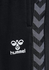 Schwarze Jogginghose mit einem weißen Logo und einem seitlichen Panel im Chevron-Muster aus kontrastierendem Schwarz- und Weißstoff. Weiches Material, normale Passform.