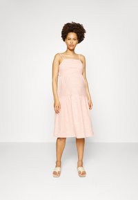 Vestido às riscas rosa com alças finas, corpete justo e saia em camadas. Textura suave e comprimento até à meia-perna. Usado com sandálias leves.