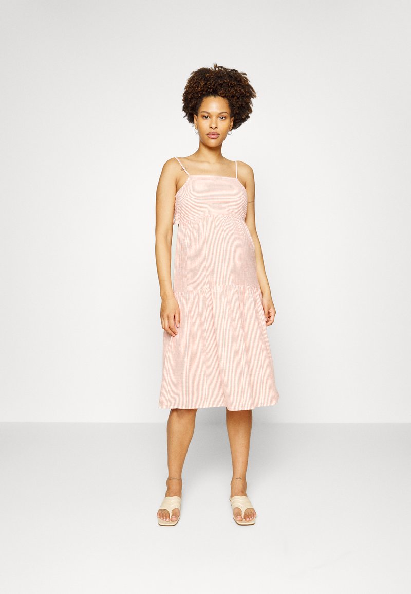 Vestido às riscas rosa com alças finas, corpete justo e saia em camadas. Textura suave e comprimento até à meia-perna. Usado com sandálias leves.