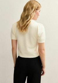 Trui met korte mouwen in crèmekleur, voorzien van een zachte, pluizige textuur. Korte snit en geribbelde zoom. Gecombineerd met zwarte, hooggetailleerde broek.