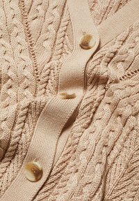 Cardigan tricoté beige clair avec motifs torsadés, doté d'un col en V et d'une rangée de boutons ronds marron clair sur le devant.