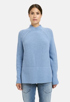 Helles blaues Strickpullover mit hohem Kragen, geripptem Saum und langen Ärmeln. Texturiertes Muster über das gesamte Stück. Kombiniert mit Jeans.