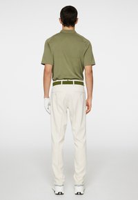 Outfit da golf per uomo: polo verde oliva, pantaloni bianchi, cintura verde, guanti bianchi, sneakers bianche. La polo ha maniche corte e colletto classico.