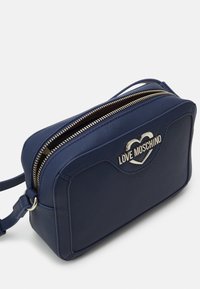 Námořnická modrá obdélníková kabelka přes rameno s stříbrným zipem a kovovým logem ve tvaru srdce "Love Moschino" na přední straně.