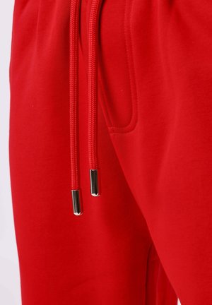 Close-up of red fabric with a pocket and two matching red drawstrings featuring silver metal tips.