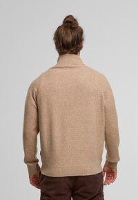 Beige wool turtleneck sweater with ribbed cuffs and hem, soft texture, relaxed fit, featuring a subtle fleck pattern.
