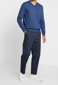 Marinblå V-ringad tröja kombinerad med marinblå och grå randiga byxor, komplett med vita sneakers. Avslappnad passform och mjuk textur.