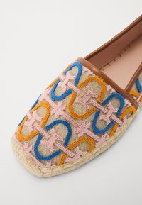 Többszínű hímzett slip-on cipő bézs alapra, kék, rózsaszín és narancssárga összefonódó mintákkal, valamint szőtt espadrille talppal.