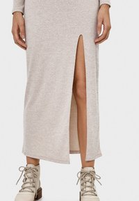 Lång, krämfärgad stickad klänning med en sidoklyvning, med ett texturerat mönster. Bärs tillsammans med beige snörda ankelboots.