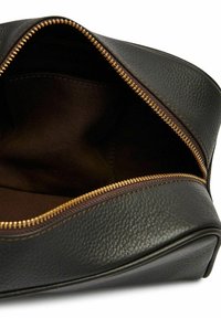 Svart läderpung med en texturerad yta, med en guldfärgad dragkedja. Invändigt fodrad med brunt tyg, vilket ger gott om förvaringsutrymme.