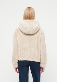 Εκρού, αφράτο πουλόβερ με κουκούλα, με άνετη εφαρμογή και ριμπ τελειώματα στα μανίκια, φτιαγμένο από μαλακό, υφασμένο υλικό.