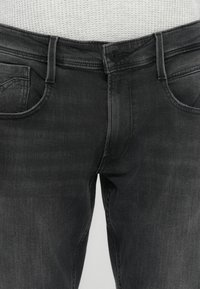 Čierne džínsy z denimu so slim fit strihom, s gombíkovým uzáverom, piatimi vreckami a jemným blednutím na textúre látky.
