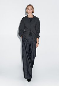Dark gray collared shirt with a loose fit, layered over a black striped top. Paired with wide-leg dark denim trousers and black shoes.