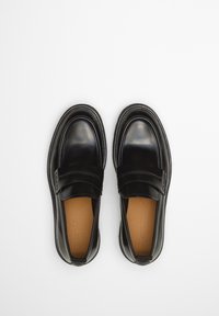 Zwarte leren instappers met een gladde textuur, ronde neus en een band over de wreef. Voorzien van een contrasterende tan kleurige binnenzool en stiksels.
