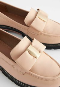 Light pink leather loafers with a rounded toe, featuring a gold-tone hardware accent, black rubber sole, and visible stitching details.