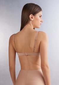 Nude bra with adjustable straps and hook closure. Smooth, minimal design, featuring a seamless band. Soft fabric with a matte finish.
