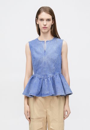 Woman wearing sleeveless blue and white striped peplum top paired with beige cargo pants, standing against a plain white background.